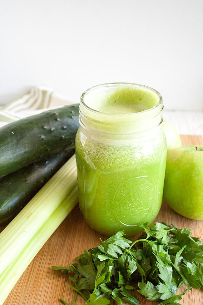 Green Detox Juice with cucumbers, apples, celery, and parsley next to it.