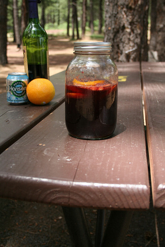 Camping Sangria on a picnic table with wine, club soda, and an orange in the background.