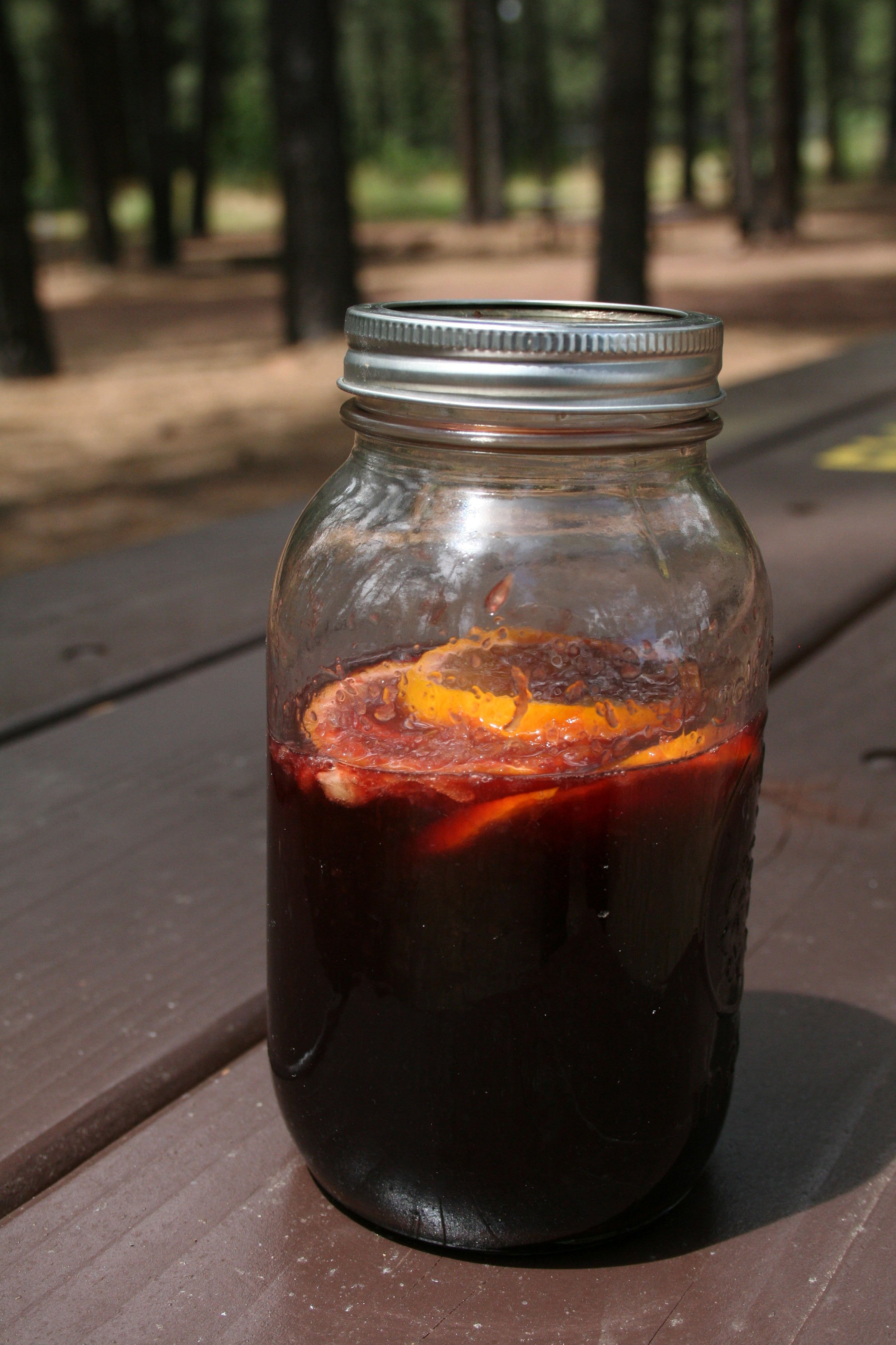 Camping Sangria in a mason jar on a picnic table in the forrest.