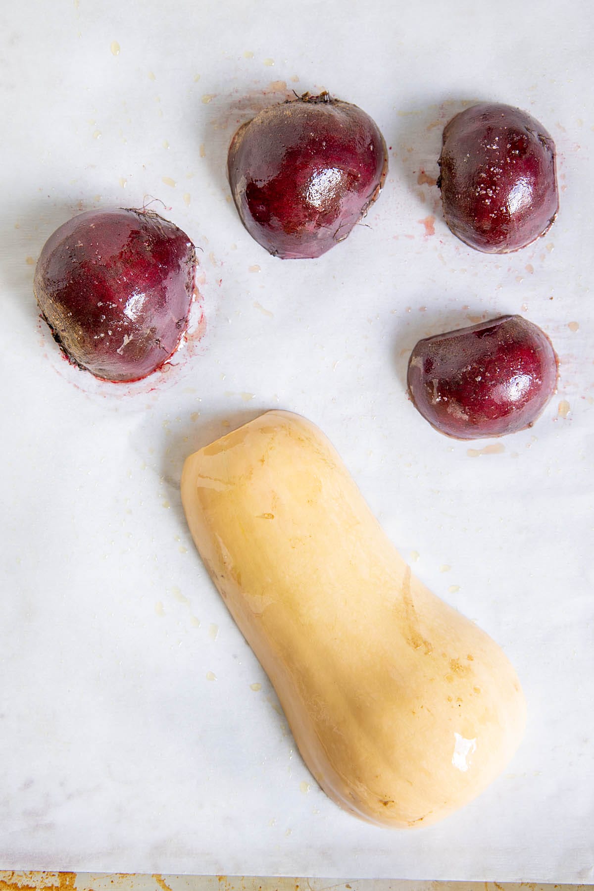 Sliced beets and butternut squash on a parchment paper lined baking sheet.