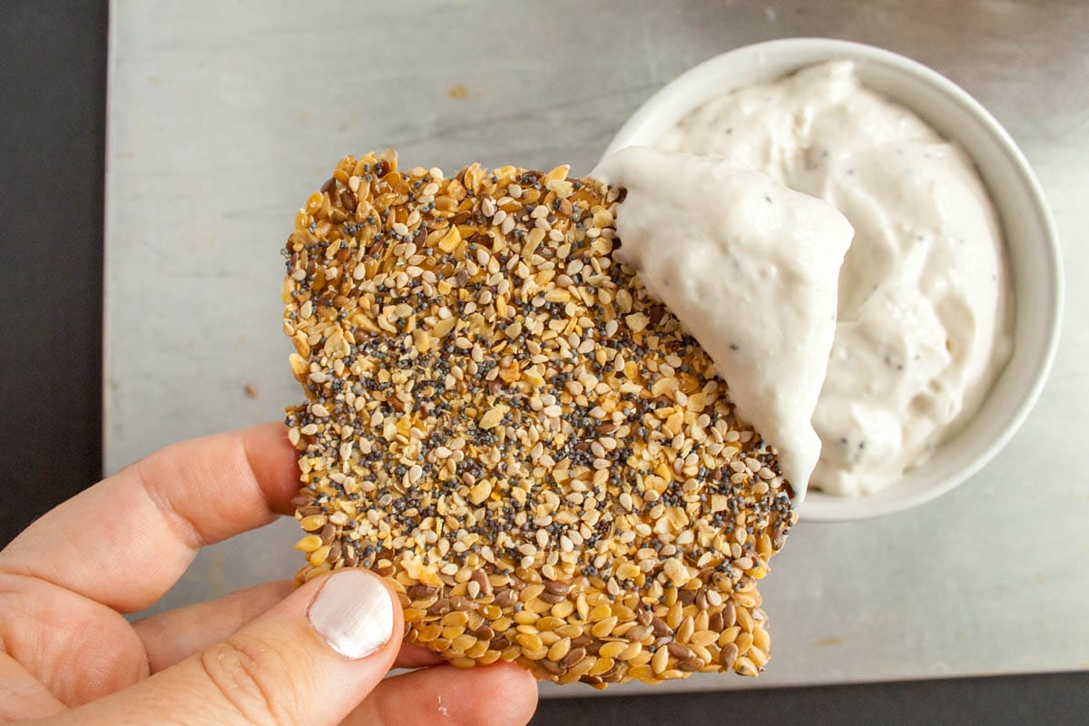 Everything Bagel Flax Cracker in hand with dip.