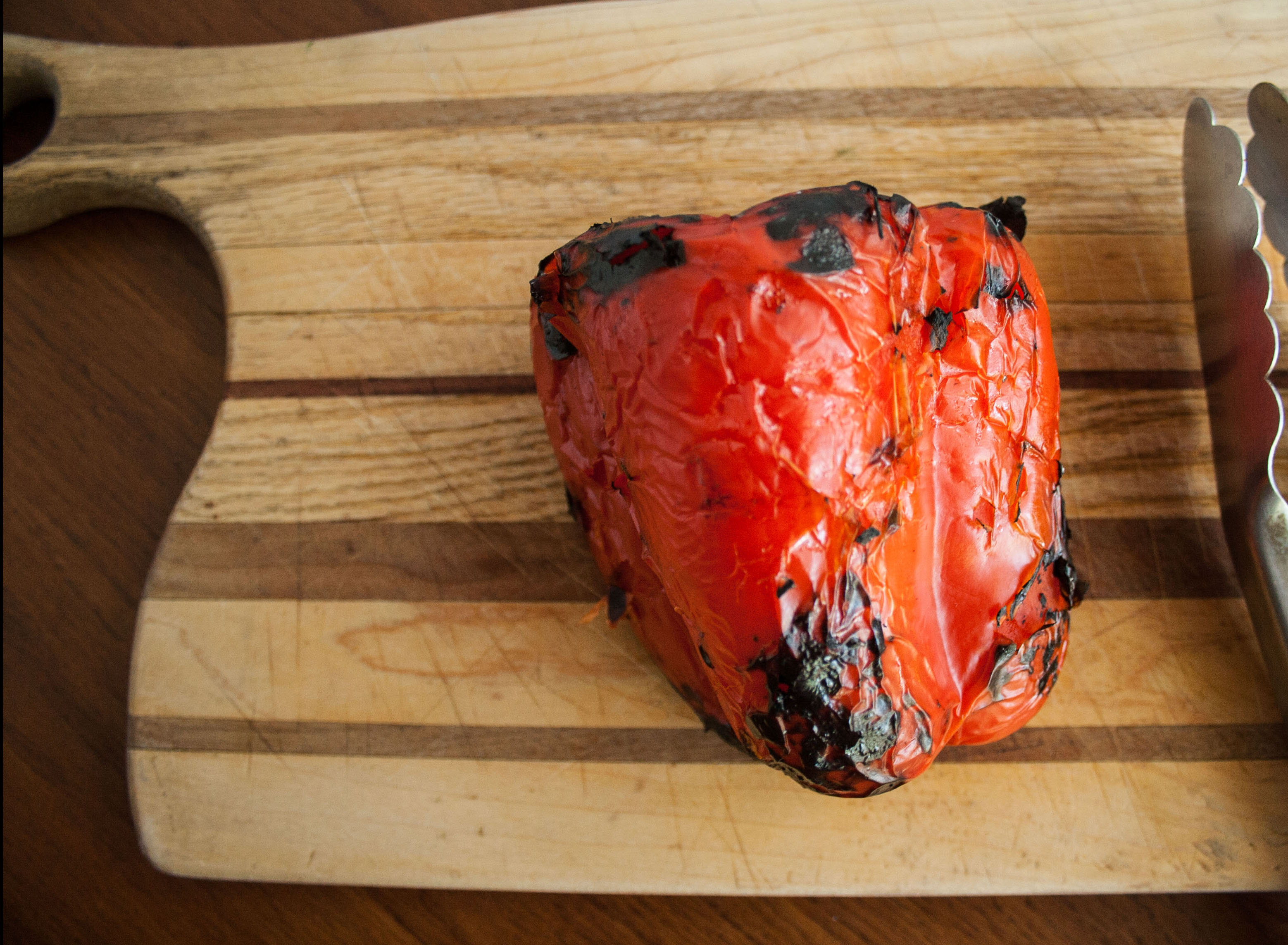 Roasted red pepper on a cutting board with tongs.