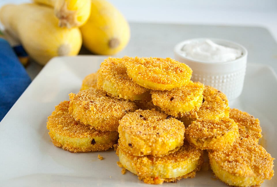 Fried Yellow Squash on a plate with vegan sour cream and yellow squash in the background.