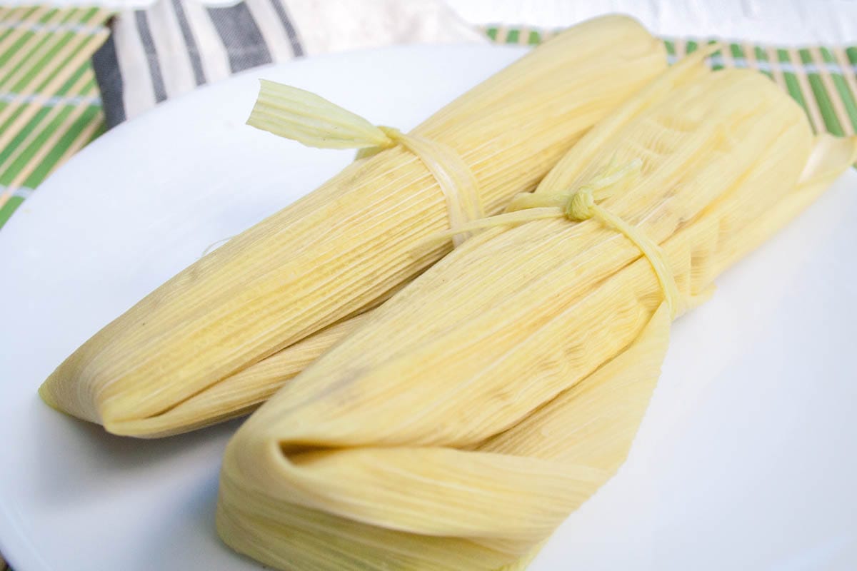 Vegan Green Corn Tamales (Tamales de Elote) - If you love Mexican food, then this recipe is for you! These rich, spicy tamales are made with Hatch green chiles, fresh white corn, and masa harina. (gluten free) Vegan Green Corn Tamales (Tamales de Elote) on a plate.