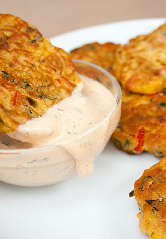 Vegetable Fritter being dipped into Vegan Chipotle Ranch Dressing. More Vegetable Fritters in background.