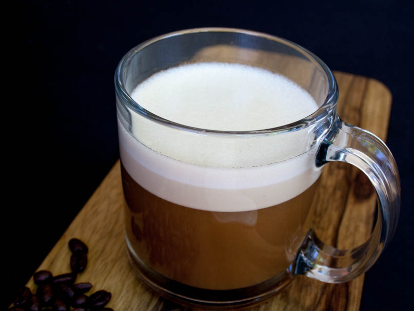 Vegan Bulletproof Coffee in a mug with coffee beans in the background.