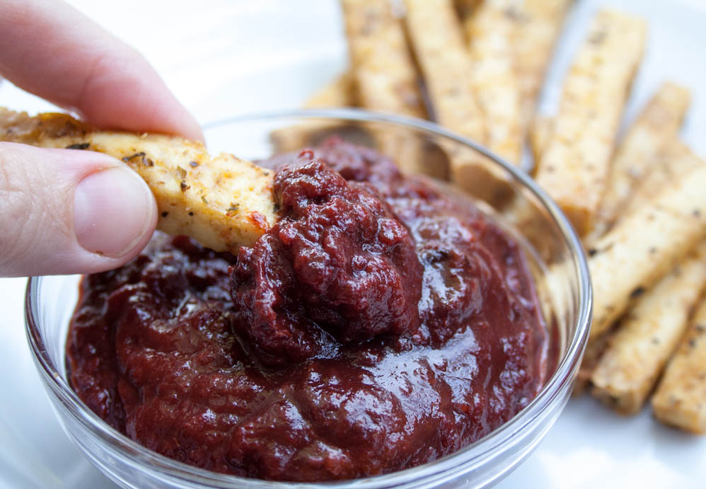 Raspberry Chipotle Ketchup with baked tofu fry being dipped in it and more fries in the background.