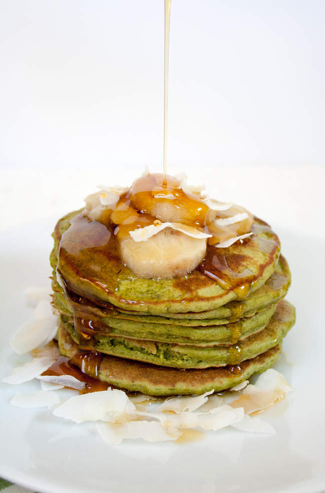 Vegan Matcha Pancakes with maple syrup being poured on top of the pancakes.