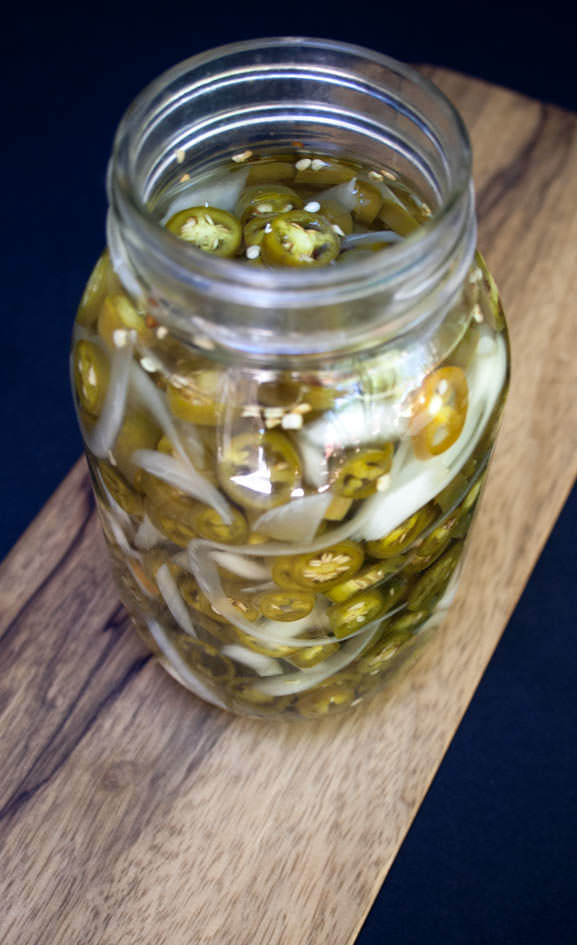 Sugar Free Pickled Peppers and Onions in a glass mason jar on a cutting board.