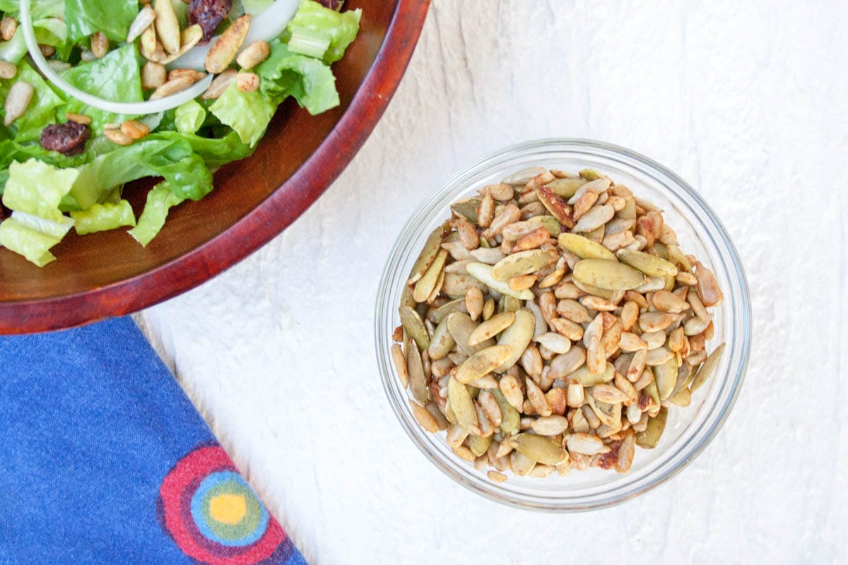 Tamari Pumpkin and Sunflower Seeds (vegan, gluten free) - This easy snack is a great addition to trail mix or a salad. Tamari elevates raw seeds to a whole new level! Tamari Pumpkin and Sunflower Seeds in a bowl next to salad.