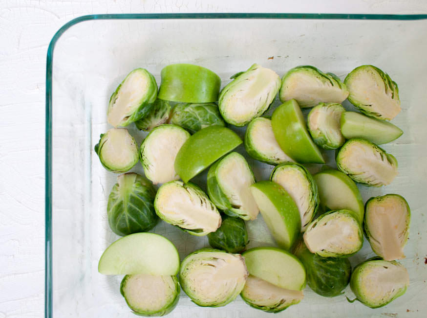 Raw Brussels Sprouts and Apples in a glass baking dish.
