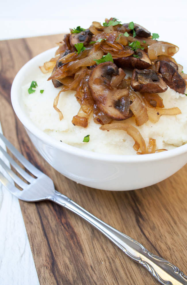 Vegan Mashed Cauliflower with Caramelized Onions and Mushrooms close up with fork on cutting board. 