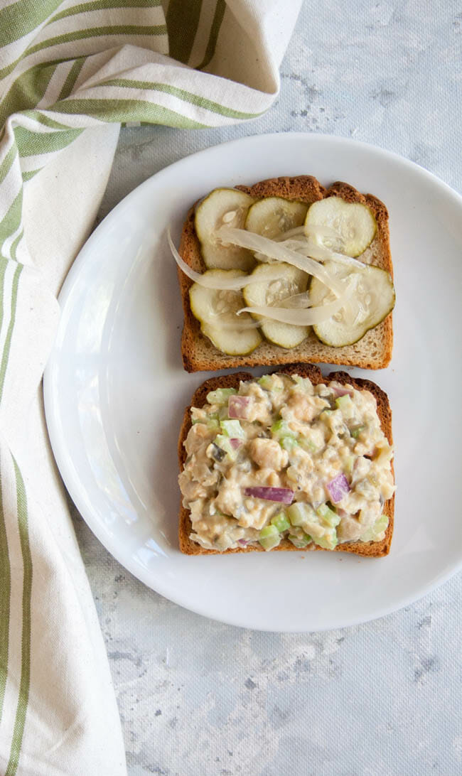 Chickpea salad spread on toast. Pickles and onions on another slice of toast.