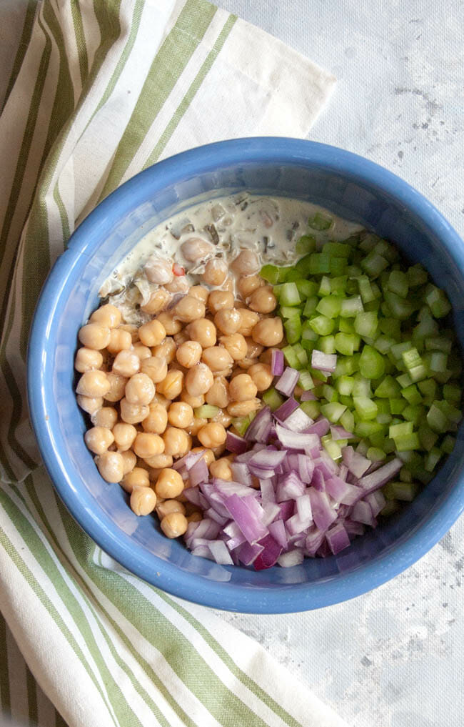 Chickpeas, chopped red onion, chopped celery and dressing in a bowl.