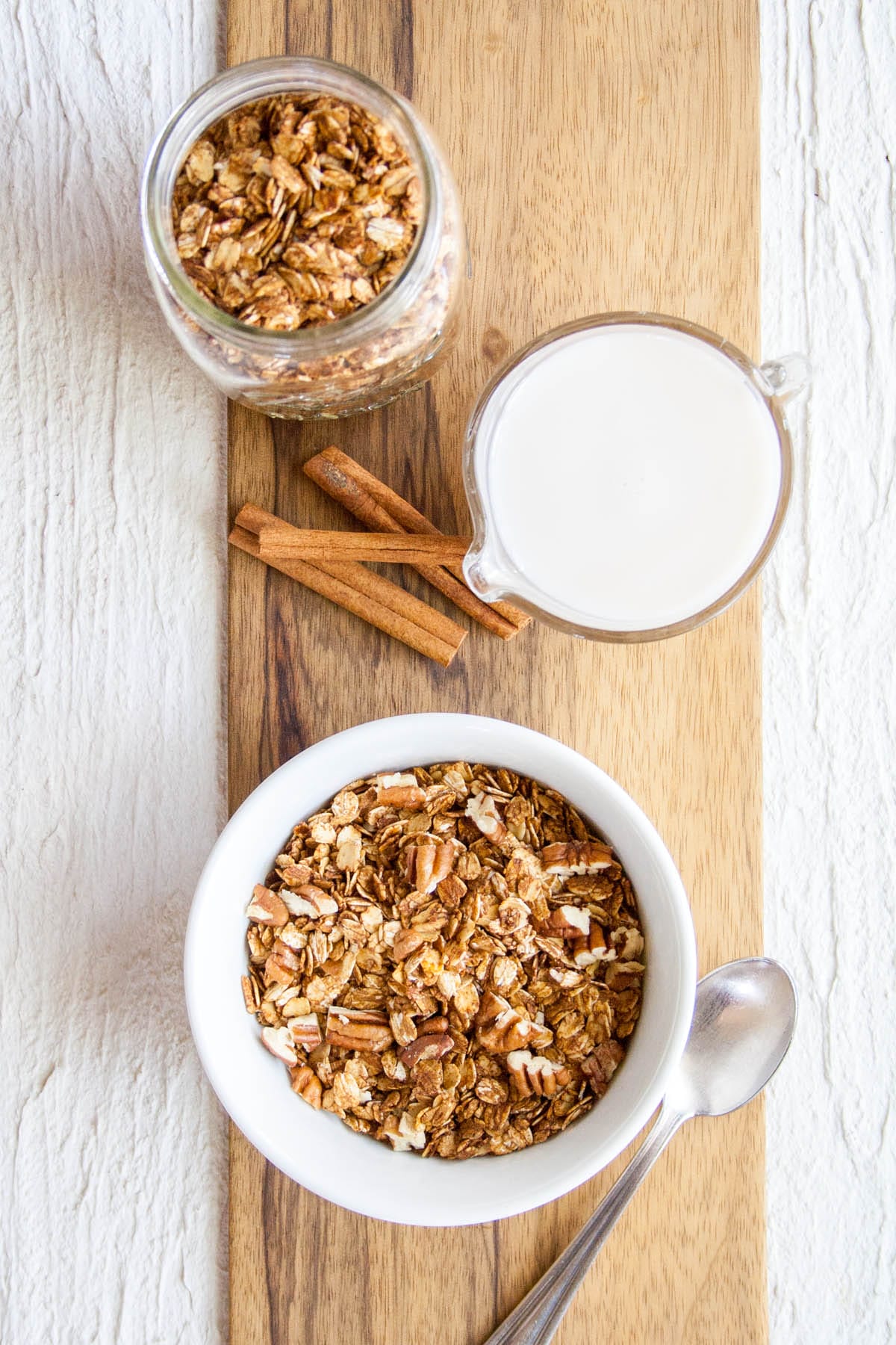 Gingerbread Granola (vegan, gluten free) - This healthy homemade granola recipe is really easy to make. It makes a lovely holiday gift or Christmas breakfast. Made with molasses, maple syrup, coconut oil, and spices. #granola #homemadegranola #homemadegifts #gingerbread #glutenfreegranola Gingerbread Granola on a cutting board with jar and pitcher.
