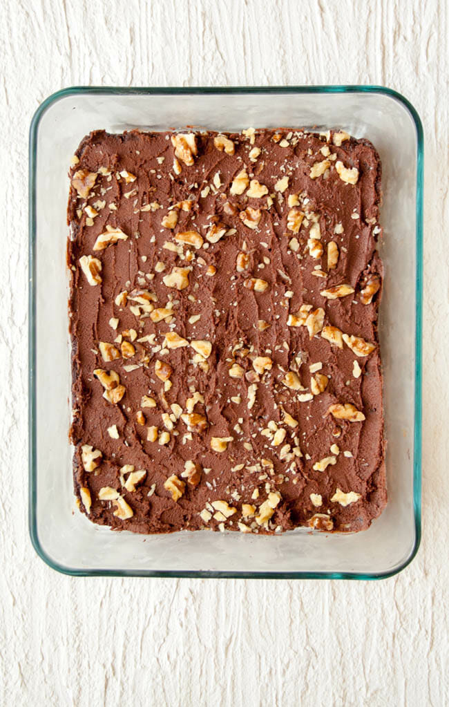 Brownies in a baking dish with frosting and walnuts.