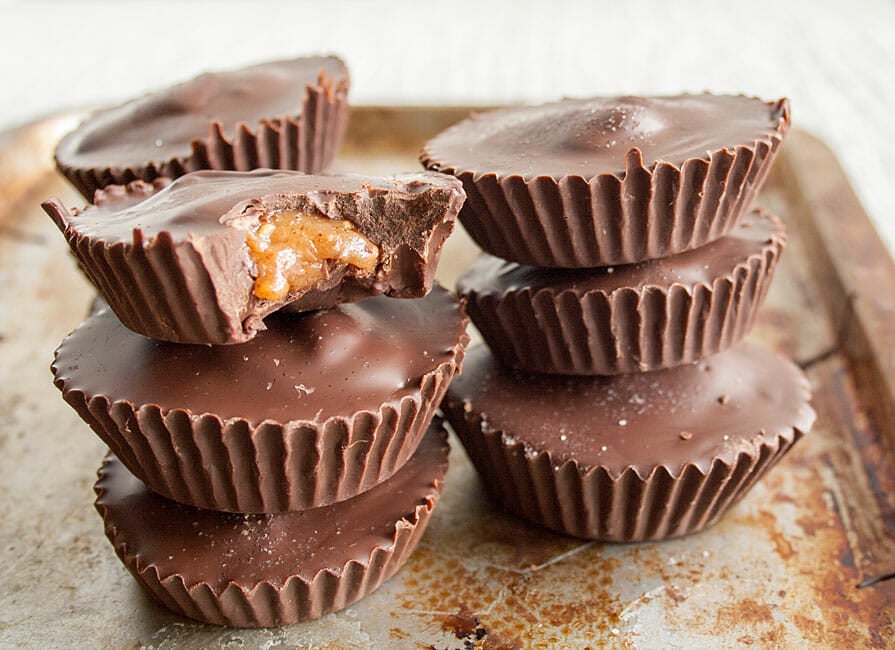Creamy Almond Butter Cups stacked on a sheet pan. One dark chocolate cup has a bite out of it.