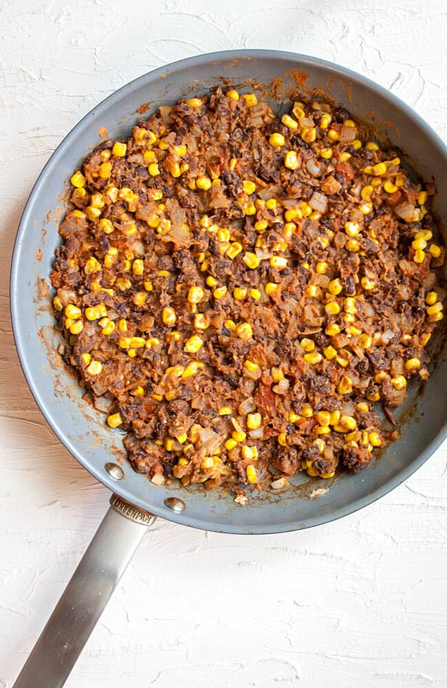 Cooked onions, garlic, black beans, and corn in a pan.