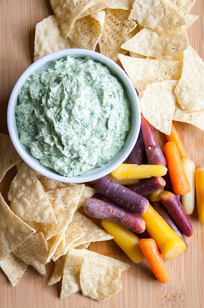 Spinach dip on a cutting board with carrots and tortilla chips.