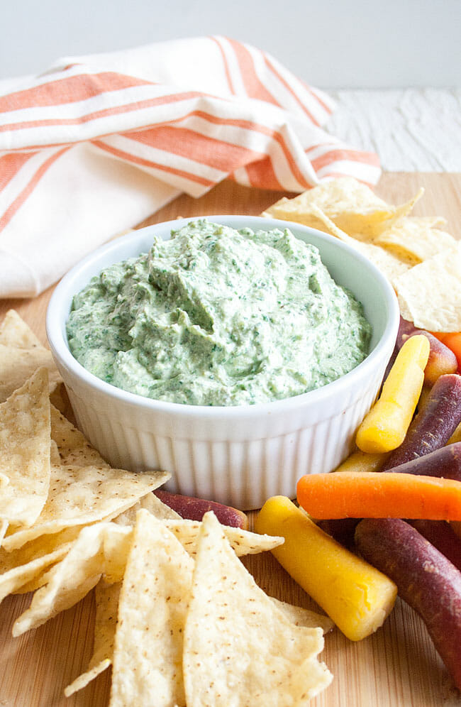 Cheesy Vegan Spinach Dip on a cutting board with tortilla chips and carrots.