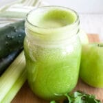 Green Detox Juice with cucumbers, apples, celery, and parsley next to it.