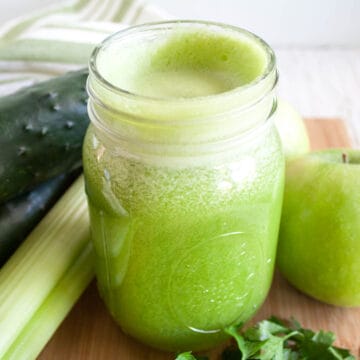 Green Detox Juice with cucumbers, apples, celery, and parsley next to it.