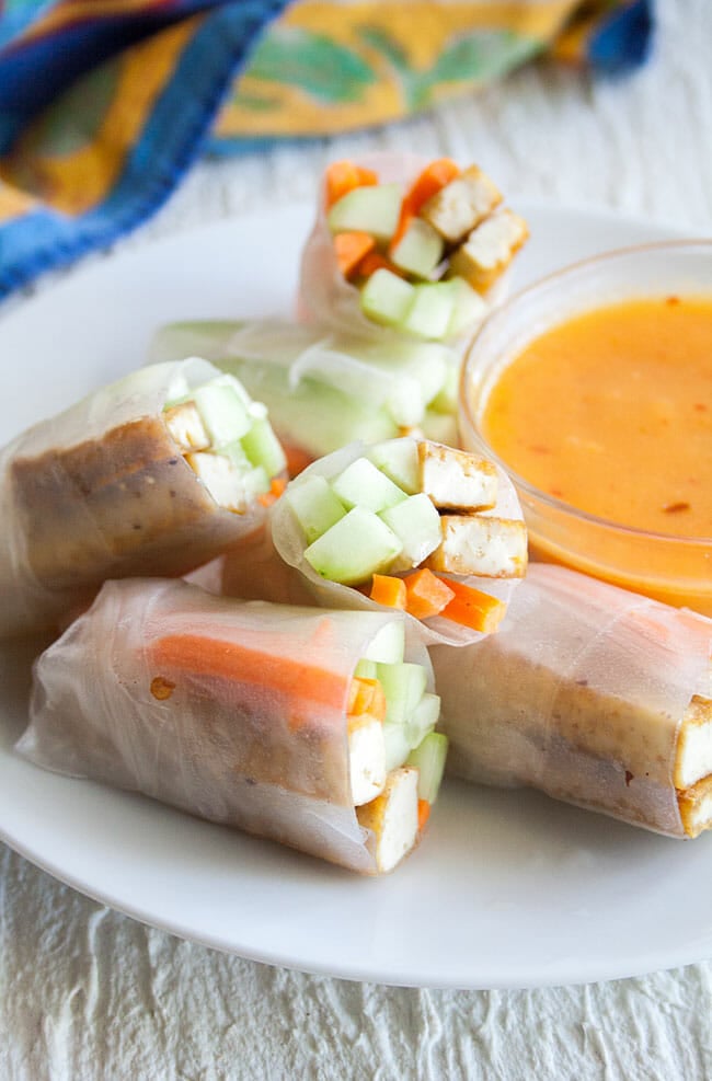 Tofu and Vegetable Spring Rolls stacked on a plate with mango dipping sauce.