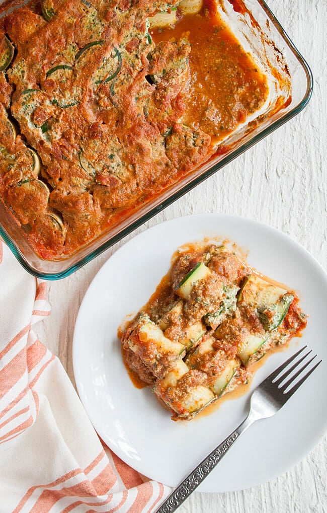 Zucchini Lasagna Rolls in a baking dish after being baked next to some on a plate.