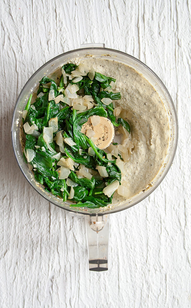 Tofu ricotta in a food processor with sauteed spinach and onions on top.