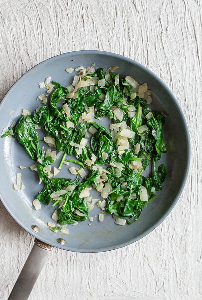 Spinach, onions, and garlic in a frying pan.