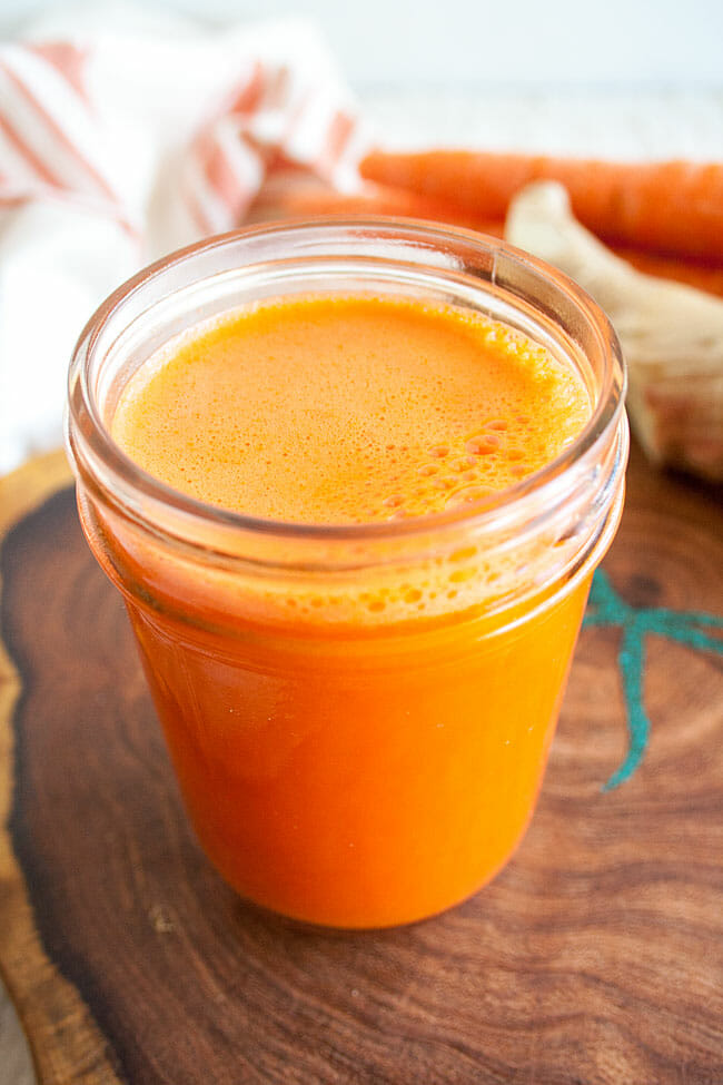 Carrot Ginger Juice with ginger and carrots in the background.