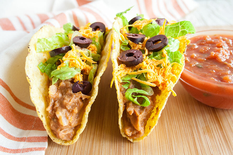 Refried Bean Tacos on a cutting board with a ramekin of salsa.