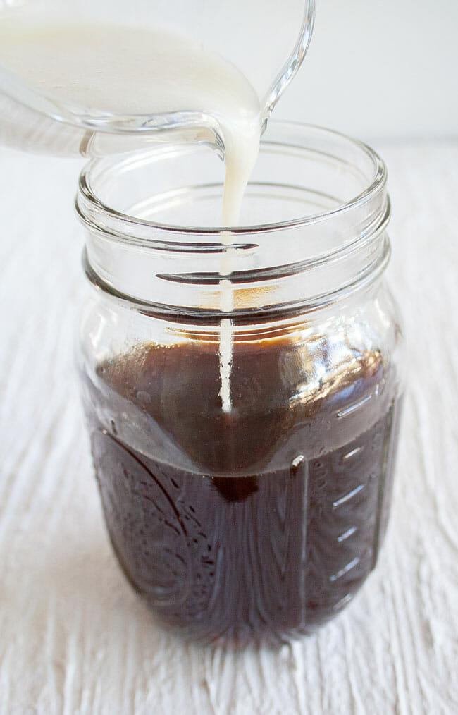 Sweetened condensed coconut milk being poured in mason jar with coffee.