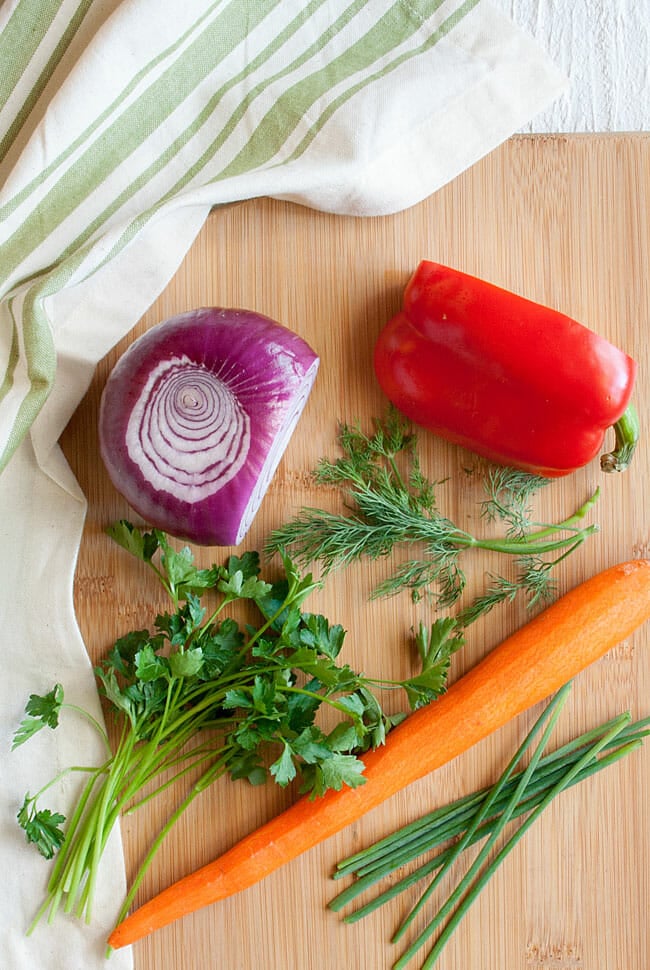 Red onion, red pepper, carrot, chives, cilantro, and dill on a cutting board.