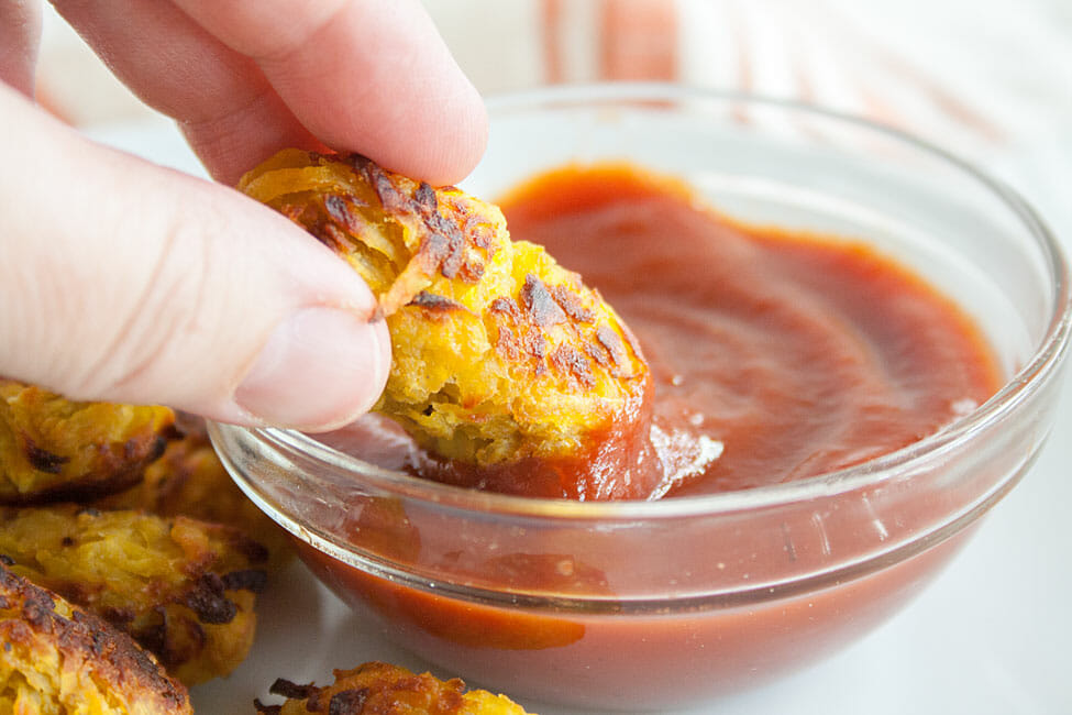 Tater Tots on a plate and one being dipped in ketchup.