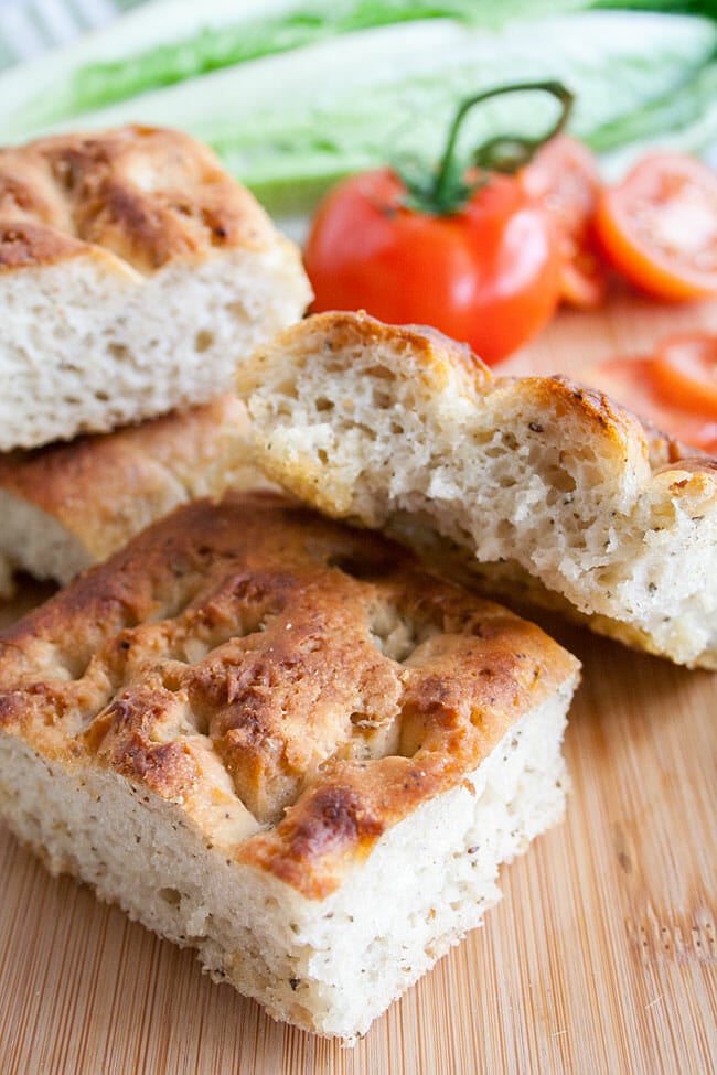 Roasted garlic focaccia on a cutting board with lettuce and tomatoes in the background.