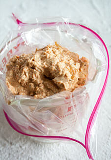 Tofu ricotta and roasted red pepper mixture in ziplock bag over measuring cup.