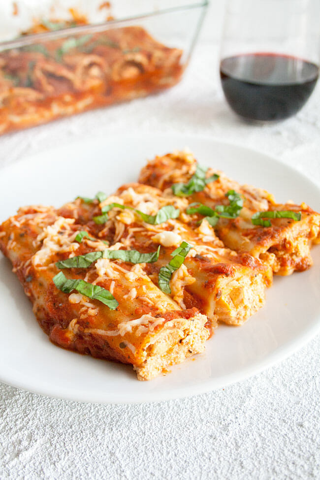 Vegan Manicotti on a plate with  a glass of wine and baking dish in the background.