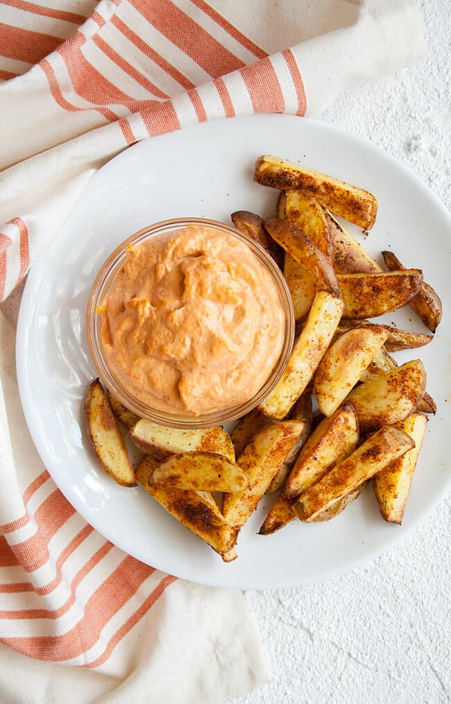 Roasted Red Pepper Dip on plate with spicy potato wedges.