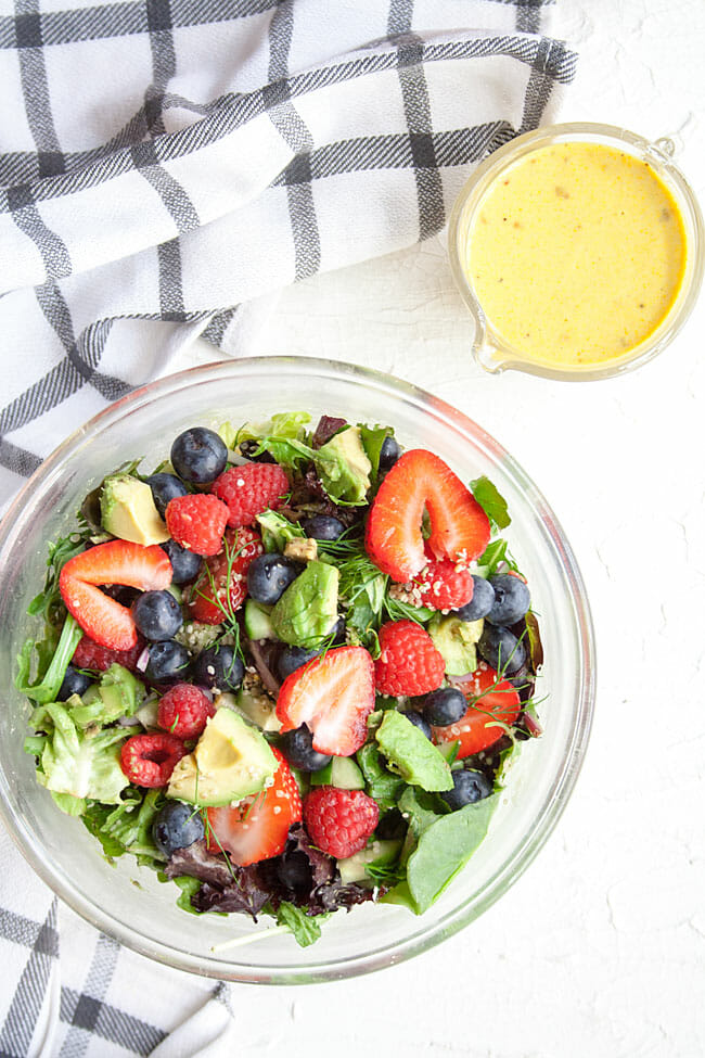 Salad in a bowl with dressing next to it in a pitcher.