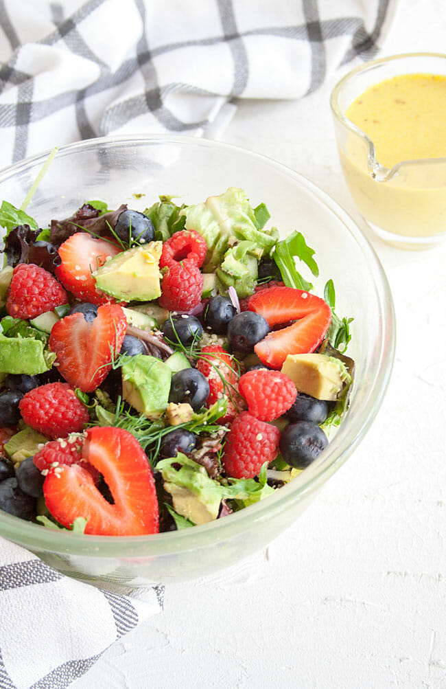 Salad in a bowl with a pitcher of dressing next to it.