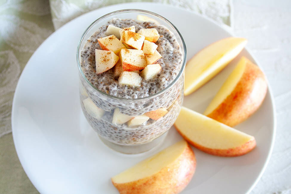 Apple Pie Chia Pudding in a small mason jar with layers of chopped apple. Apple slices on a plate in the background.