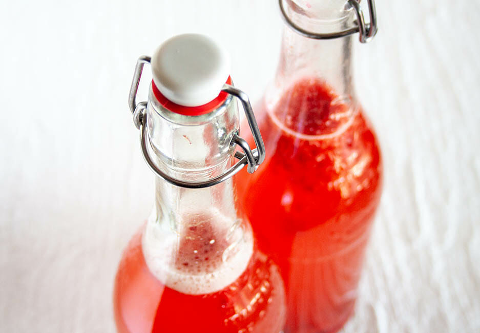 Raspberry Kombucha in two pop top bottles close up.