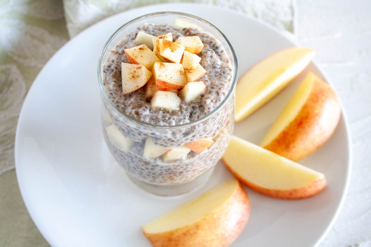 Apple Cinnamon Chia Pudding (vegan, gluten free) - This quick and easy recipe is a healthy breakfast or snack. Make it ahead of time for a meal on the go! #chiapudding #veganchiapudding Apple Cinnamon Chia Pudding in a jar with sliced apples on a plate.