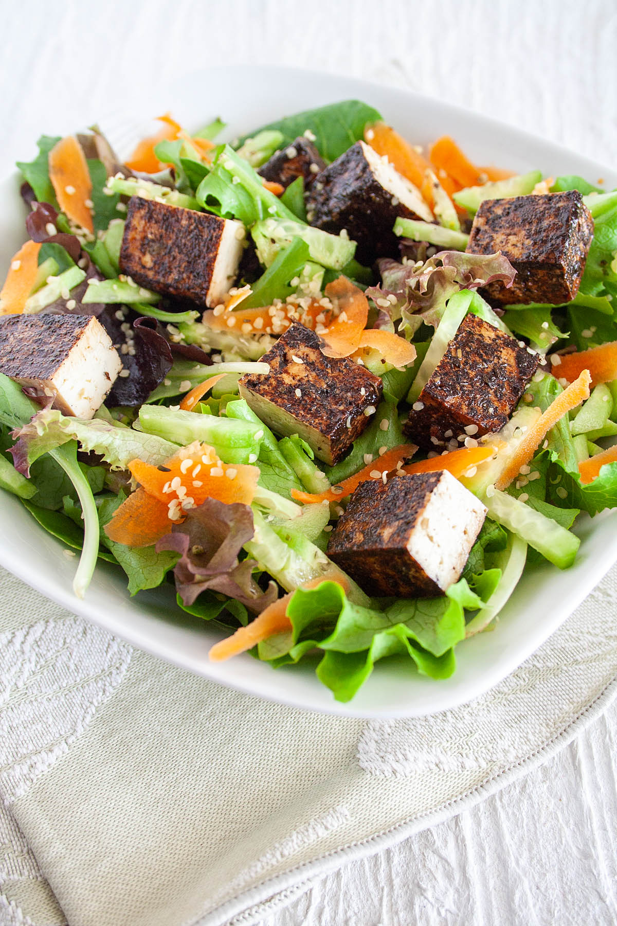 Balsamic Tofu on a salad with sliced carrot and hemp seeds.