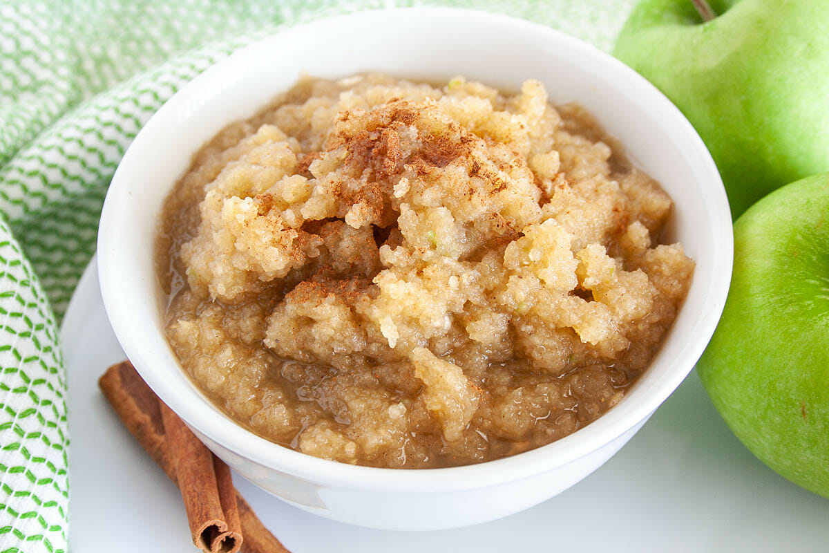 Green Raw Applesauce in a bowl with Granny Smith apples next to it.