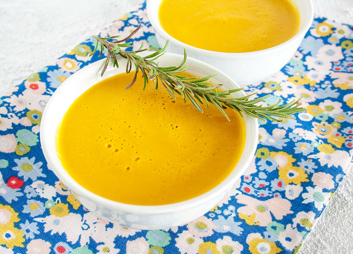Creamy Sweet Potato Rosemary Soup in two bowls with sprig of rosemary.