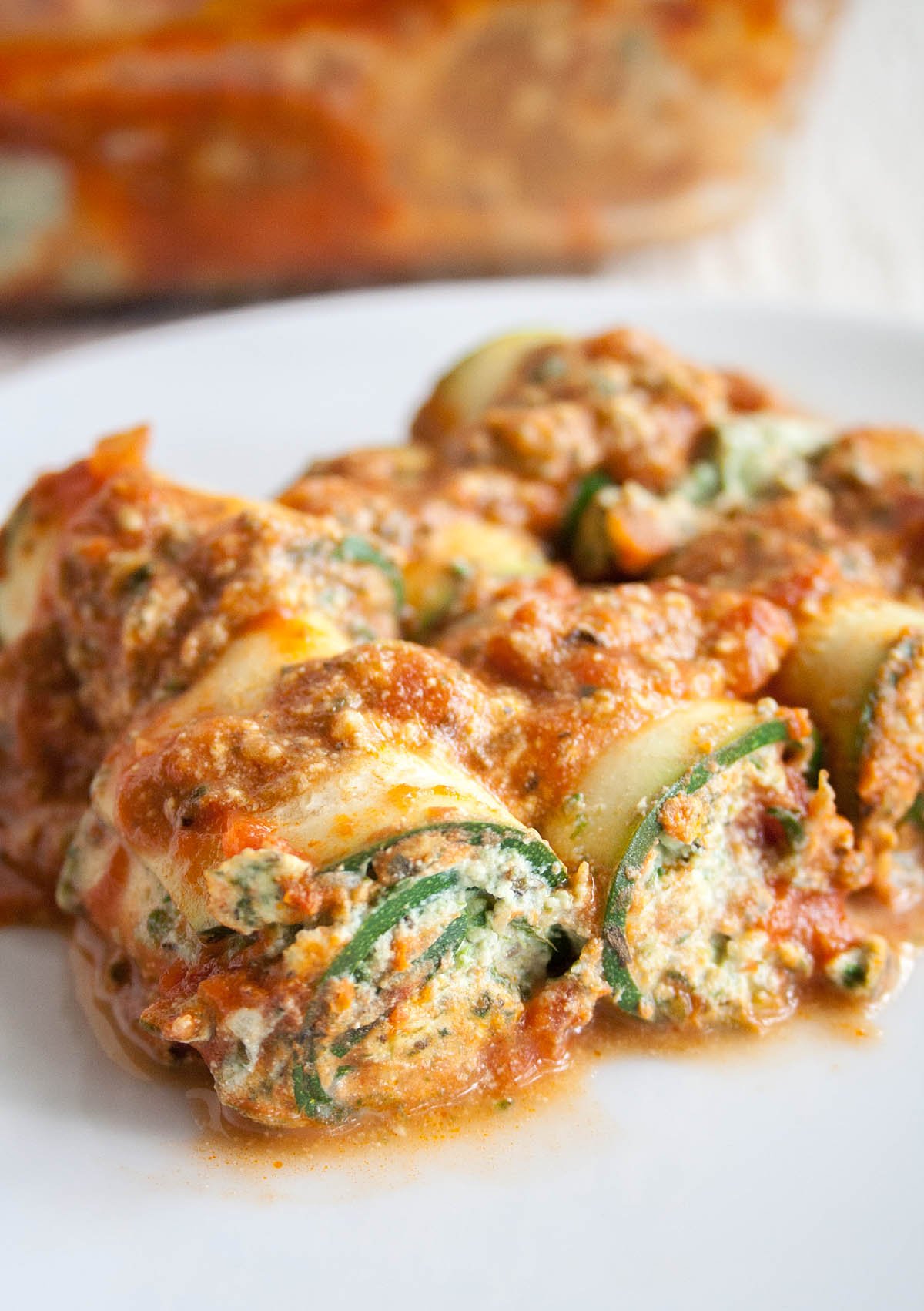 Zucchini Lasagna Roll-Ups on a plate with baking dish in the background.