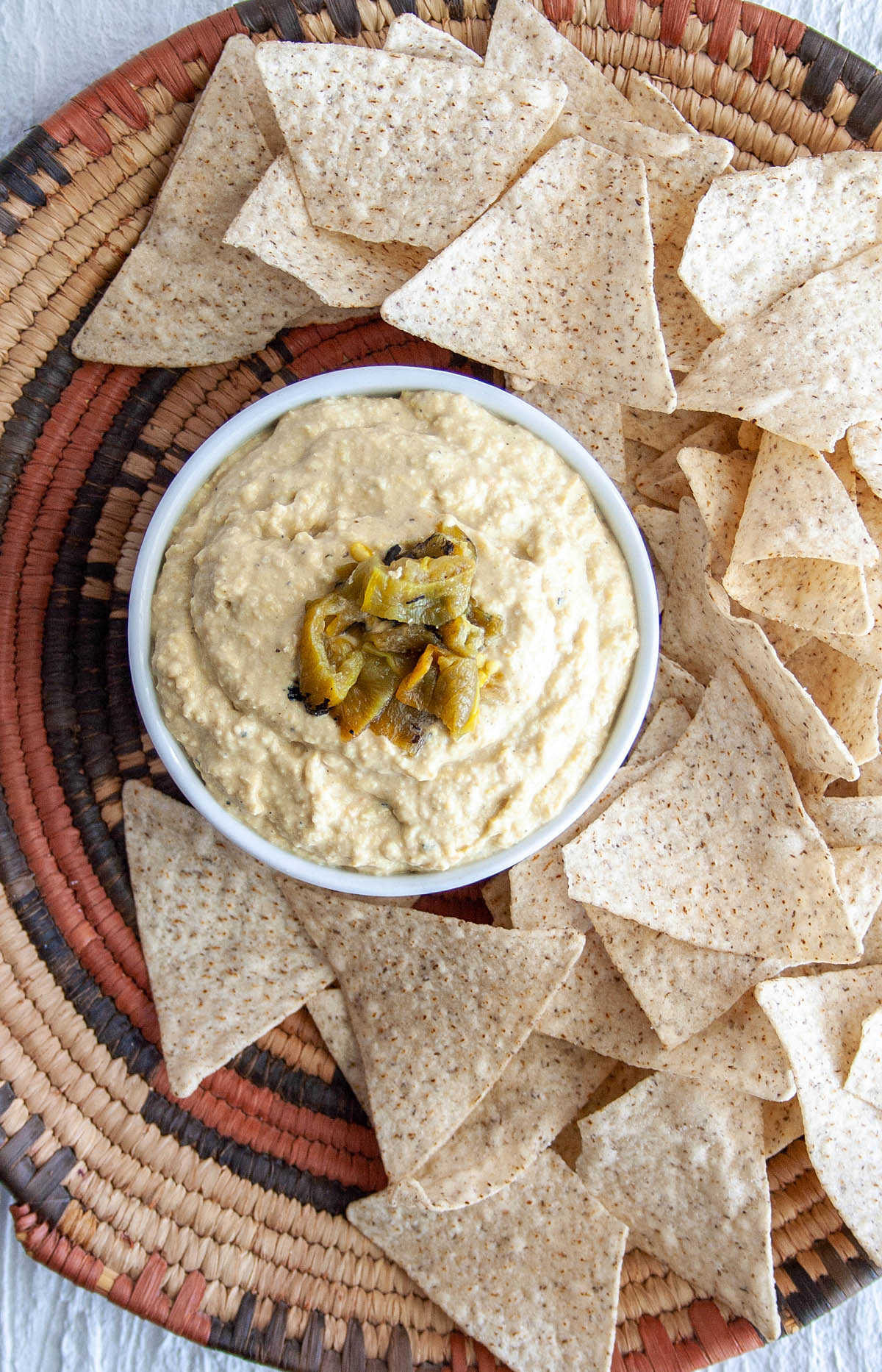 Roasted Hatch Chile Hummus with chopped Hatch pepper on top and tortilla chips in a basket.