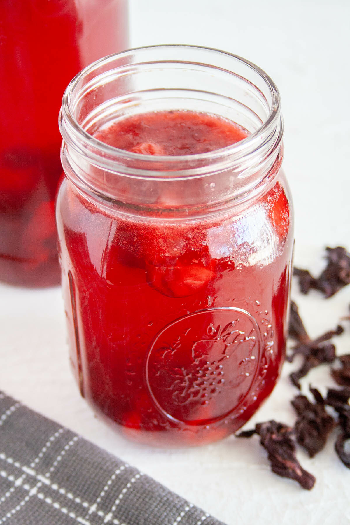 Cherry Hibiscus Kombucha in a mason jar with hibiscus flowers.